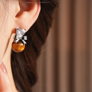 Detail view of heart zircon and silver bow earring with tiger eye bead on model