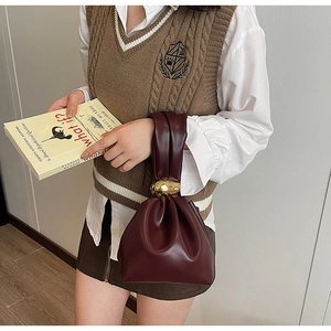 Detail of burgundy drawstring bucket bag with a large gold metal buckle and pleats