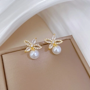 Macro detail of gold flower earrings featuring sparkling zircon inlay and a white pearl drop