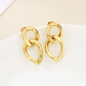 Macro view of gold minimalist twisted cuban link chain earrings on ceramic rim