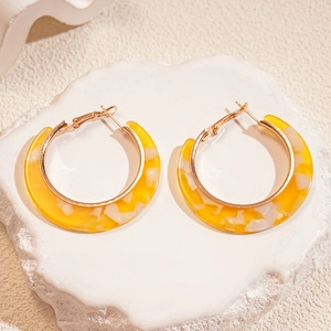Detail view of yellow and white tortoiseshell C-shaped earrings on a plaster stone base