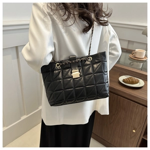 Fashionable black quilted tote bag with gold chain strap worn with a white blazer