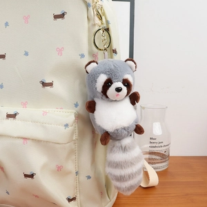 Cute raccoon plush keychain charm with striped tail hanging on a beige backpack