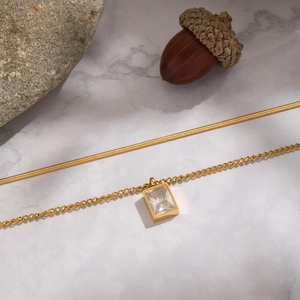 Détail du collier double couche plaqué or 18K avec zircon carré sur fond de marbre