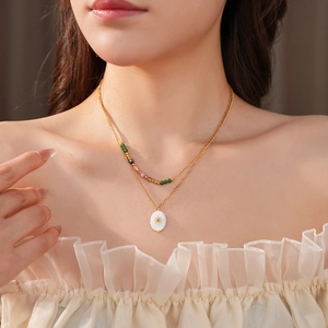 Detail of layered gold necklace with colorful beads and white oval sunburst pendant