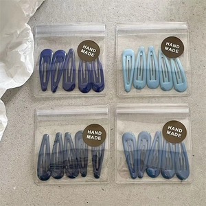 Macro detail of 20 blue gradient drop hair clips in four handmade packs on grey stone