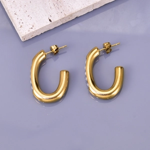 Macro shot of gold U-shaped stud earrings with inlaid pearls on a lavender surface