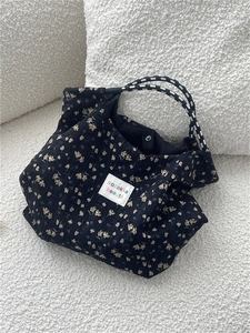 Close-up of floral canvas tote bag with woven rope handles and brand label on white texture