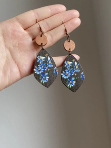 Detail of wooden teardrop earrings featuring blue and white daisy floral patterns