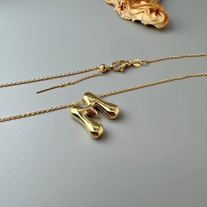 Polished gold M-letter pendant necklace with adjustable chain on minimalist background
