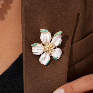 Detailed view of a flower brooch with white enamel petals and turquoise beads on a brown blazer