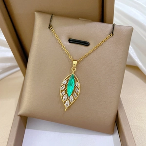 Detail shot of a golden leaf pendant with a green gemstone and sparkling zircon crystals