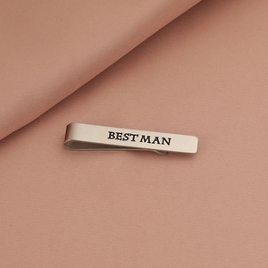 Detailed view of silver tie clip with Best Man engraving on a pink textured background