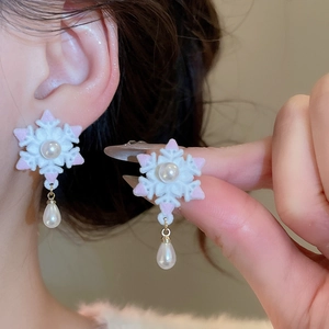 Détail de boucles d'oreilles flocon avec peluche, perles et touches de rose