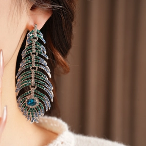 Macro shot of long feather earrings featuring emerald and blue crystals in a silver setting