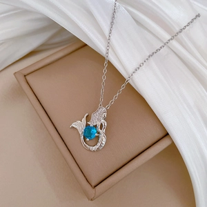 Macro shot of silver mermaid pendant with a blue gemstone on white silk fabric