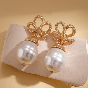 Detail of vintage gold bow earrings with baroque pearls on a warm stone background