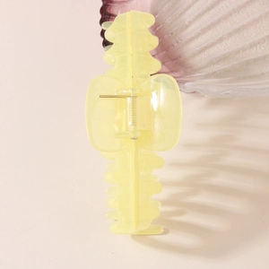 Elegant yellow translucent jelly claw clip on a beige surface with a seashell accent