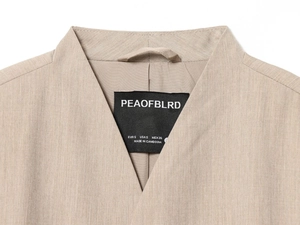 Detail of khaki blazer collar and fabric texture with PEAOFBLRD brand label and size tag