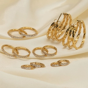 Set of gold titanium steel hoop earrings with zircon stones on silk background