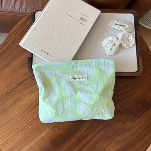 Macro detail of light green pleated mesh cosmetic bag with simple wish label on wood table