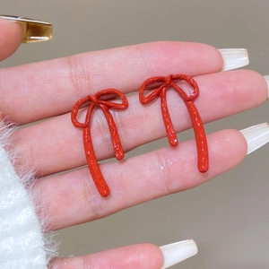 Detailed close-up of red bow-knot stud earrings with textured matte finish held in hand