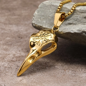 Detailed view of golden viking raven skull necklace with runes on a grey stone texture