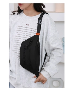 Detail of black nylon chest bag with orange buckle on strap and minimalist branding