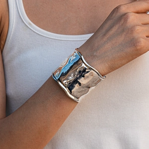 Detailed close-up of wide textured silver bangle with liquid metal hammered ripple effect