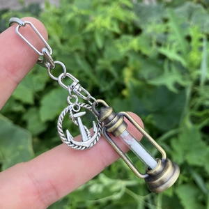 Detail of silver anchor and bronze hourglass charm with white sand on a metal keychain