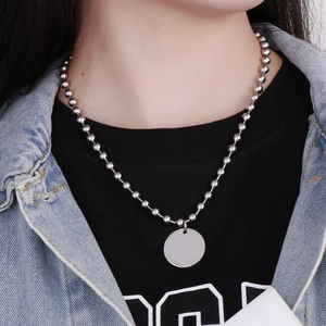 Détail d'un collier à billes argenté avec un pendentif rond poli porté par un mannequin
