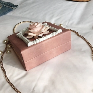 Detailed view of pink rose box bag with floral frame and gold chain on fabric