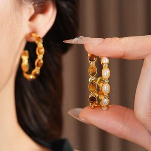 Dettaglio macro di orecchini vintage placcati oro con occhio di tigre e perle