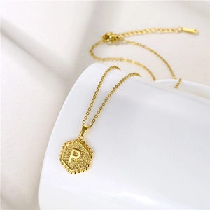 Detail view of gold hexagonal necklace with letter P engraving on white ceramic