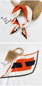 Detail view of a pleated silk scarf in orange, black, and white tricolor geometric pattern