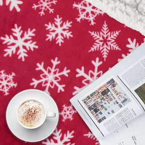 Close-up of red Christmas blanket with white snowflake pattern and cozy coffee mug