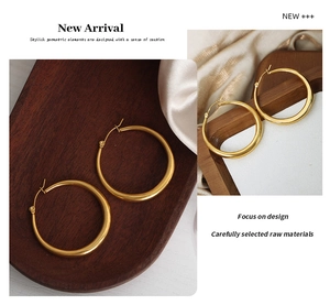 Detailed close-up of chunky gold hoop earrings on a textured wooden tray and silk fabric