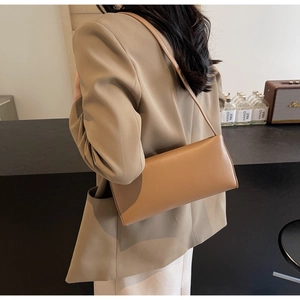 Chic brown leather baguette bag styled as an underarm shoulder bag on a female model