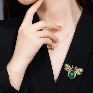 Elegant gold bee brooch with green gemstone and sparkling white crystals on black clothing