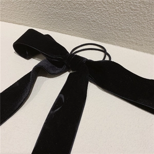 Detailed close-up of a large black velvet bow hair tie with elegant long velvet ribbons