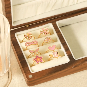 Macro shot of assorted pink enamel charms and stainless steel rings in a wooden box