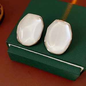 Macro shot of minimalist white resin oval earrings with elegant gold borders on a gift box