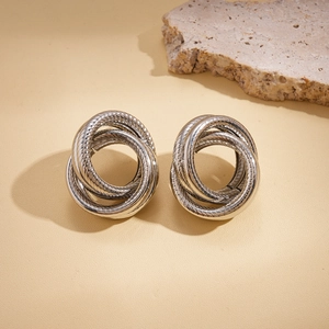 Close-up of silver geometric multi-layer intertwined loop earrings on textured stone