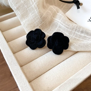 Close-up of black velvet camellia earrings with subtle logo detail on a white jewelry tray