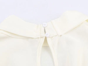 Detail van de crème jurk met twee knopen en een druppelvormige uitsnede bij de halslijn