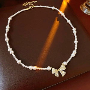 Detail of pearl necklace featuring a golden bow pendant with zircons on leather