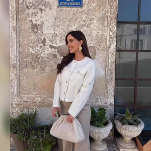Women's white tweed jacket styled with a shearling clutch bag in a European street setting