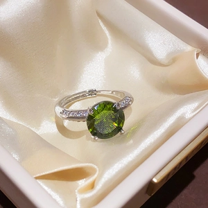 Macro shot of silver ring with large green zircon and pave white stones on satin