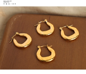 Detailed view of four irregular wavy gold earrings on a rustic wooden base and fabric