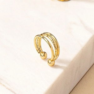 Golden non-piercing three-layer ear cuff with round metal beads on white marble surface